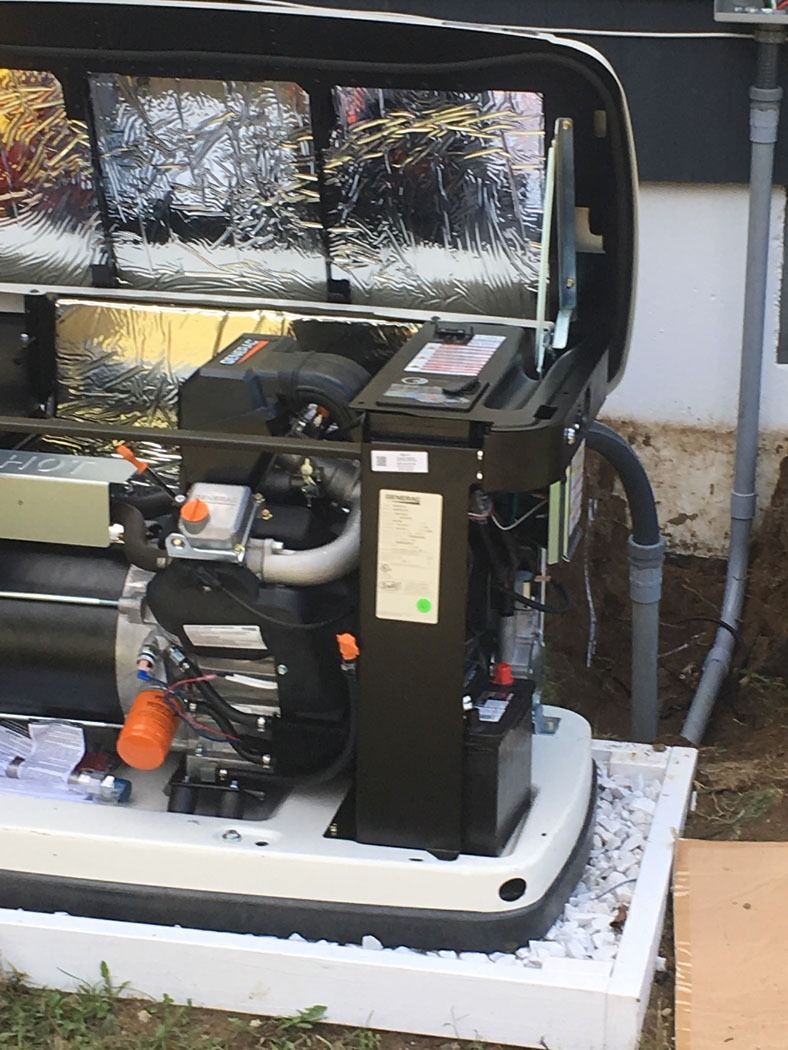 Portable generator with black frame and white base, sitting outdoors beside a wall and a hose.