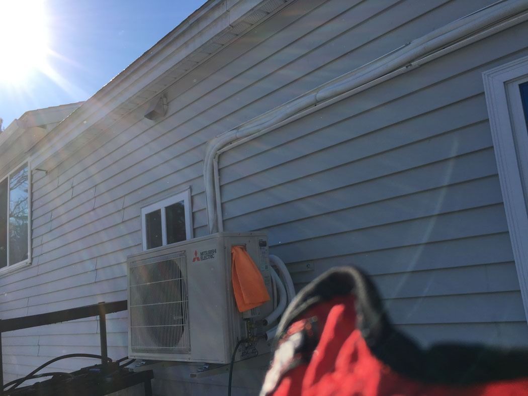 Side of a house with vinyl siding, an air conditioner, and a red-black glove in the foreground.