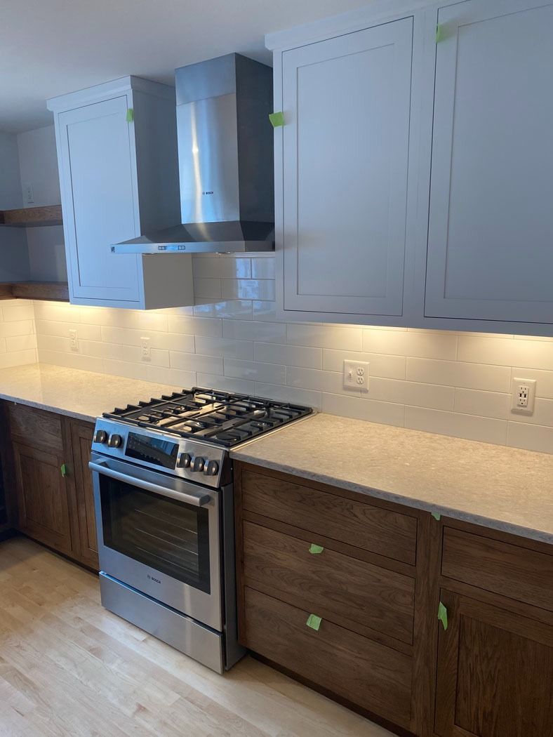 Modern kitchen with stainless stove, white cabinets, wood lower cabinets, and beige countertop