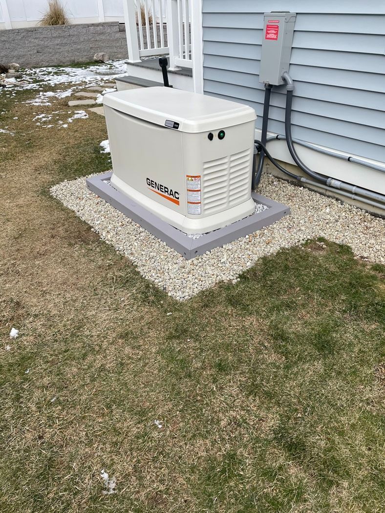 White generator on a concrete pad beside a house with gray siding and gravel landscaping