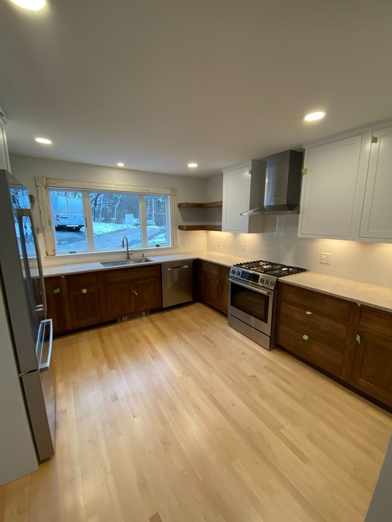 Modern kitchen with wood cabinets, stainless appliances, large window, and light wood floor