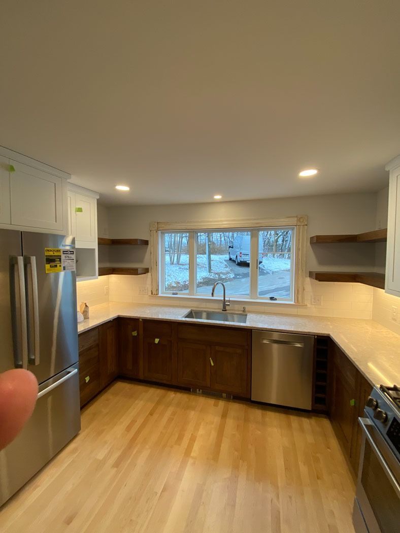 Bright kitchen with white cabinets, stainless fridge, wood floors, and a window over the sink.
