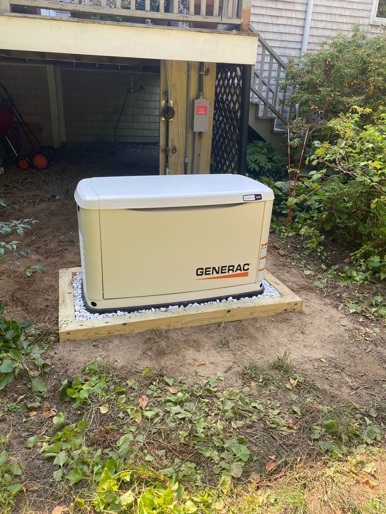Beige Generac generator on a concrete pad beside a house and garage in a yard.