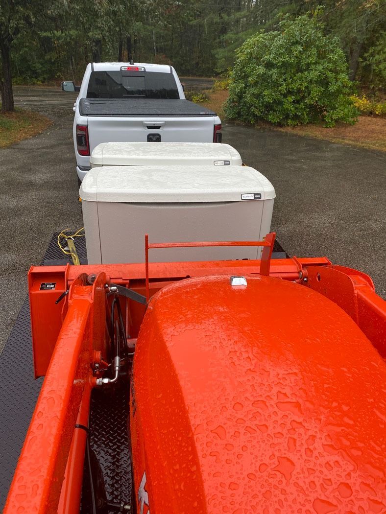 View from a truck towing white cargo trailers behind a white pickup on a wet road in a wooded area