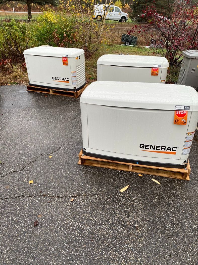 Three white Generac generators on wooden pallets in a wet driveway outdoors