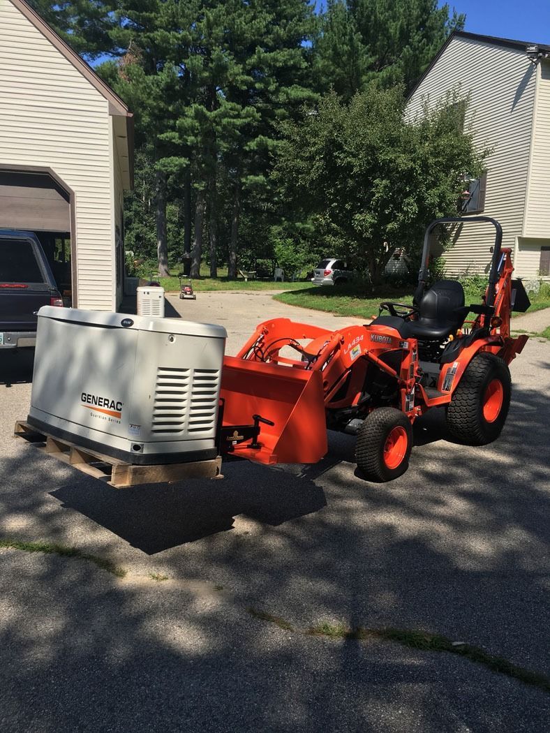 Orange tractor with front loader towing a white utility unit on a driveway between houses