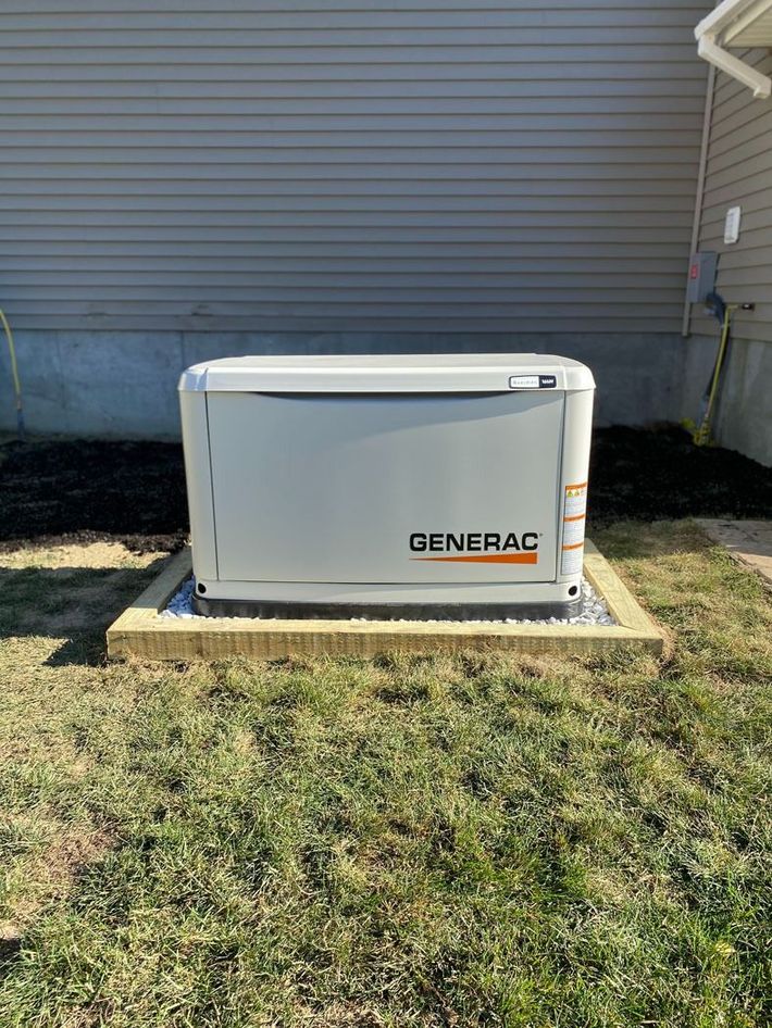 White Generac generator on a concrete pad beside a house with gray siding.