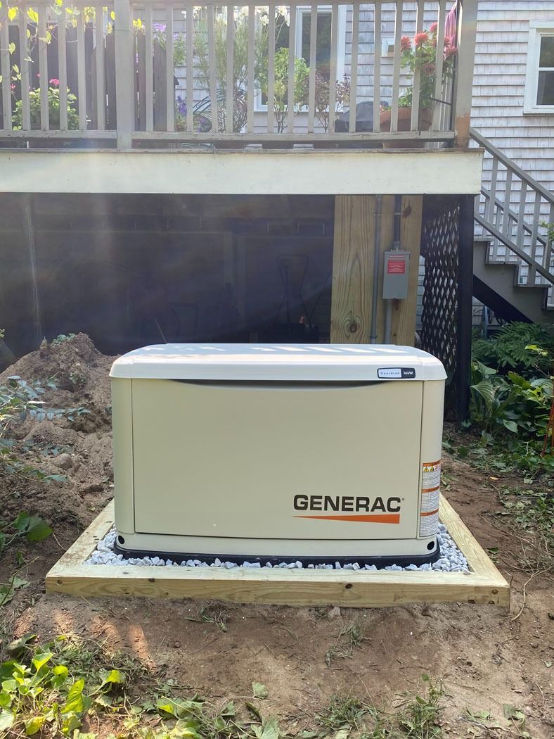 Beige Generac backup generator on a concrete pad beside a house with a deck and stairs.