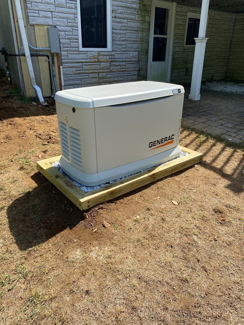Outdoor standby generator beside a stone house, set on a wooden platform in a dirt yard.