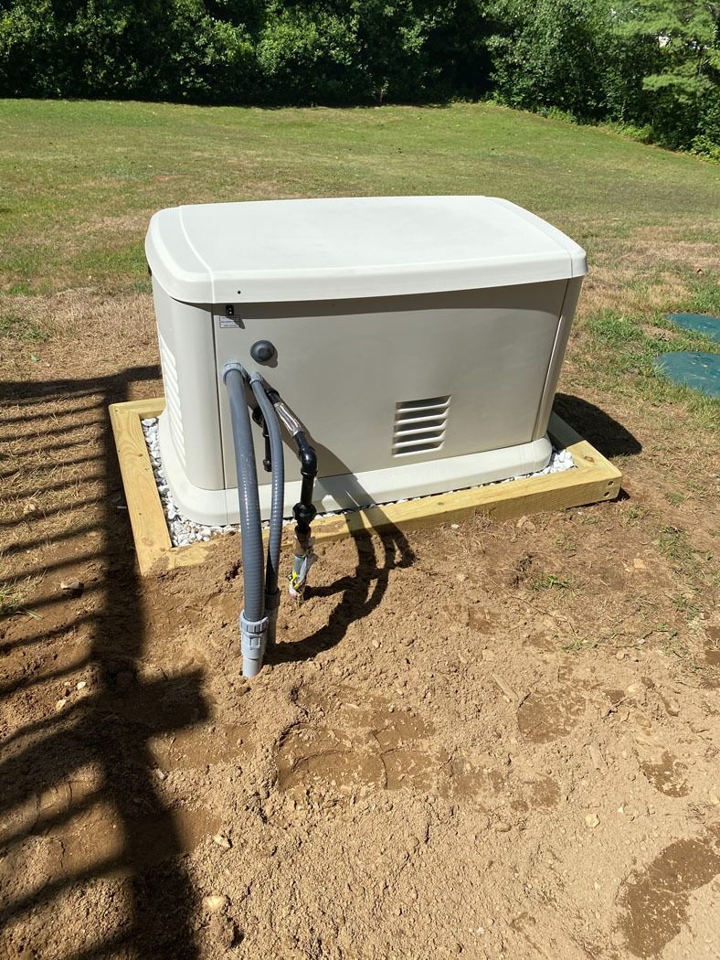 White outdoor generator or utility box beside a house, with hoses and pipes on a concrete pad in a grassy yard.