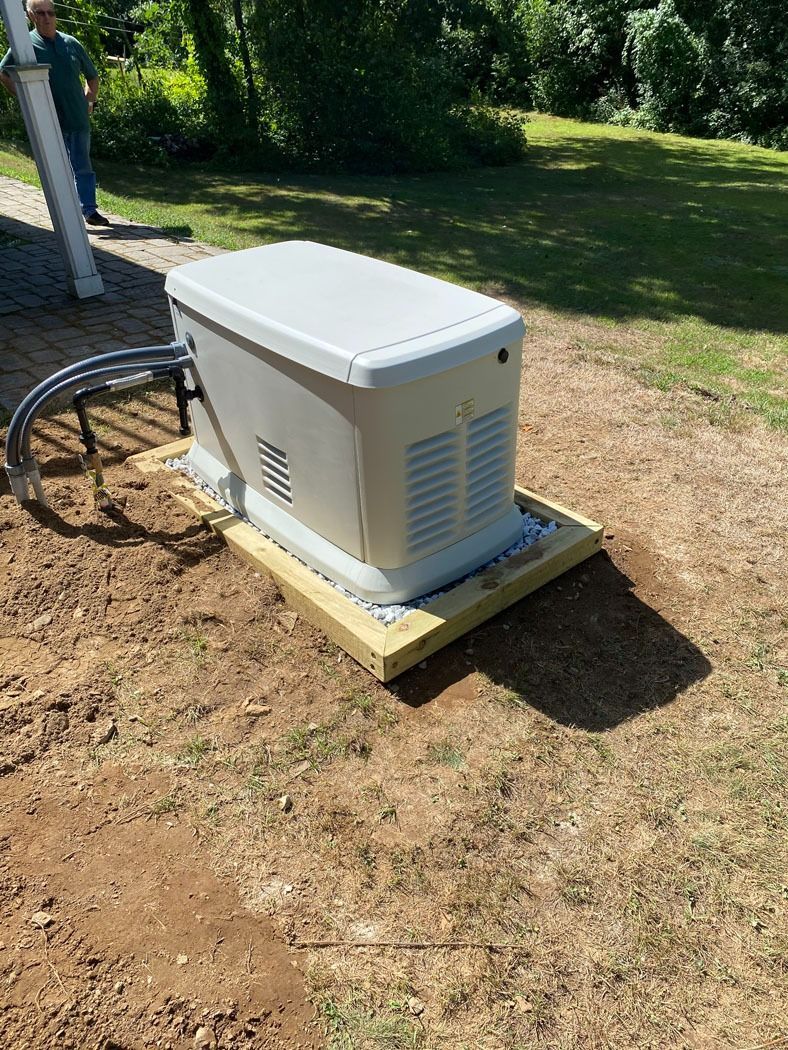 Outdoor backup generator on a concrete pad beside a house in a grassy yard