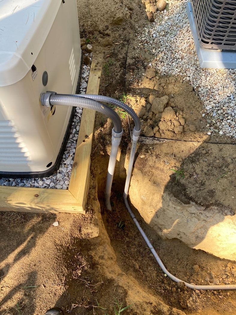 Flexible black cable entering a white electrical box beside a dirt trench and concrete foundation