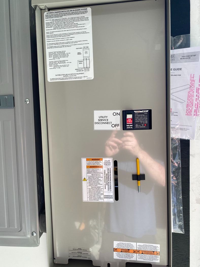 Gray utility panel with warning labels and a reflection of a person taking the photo