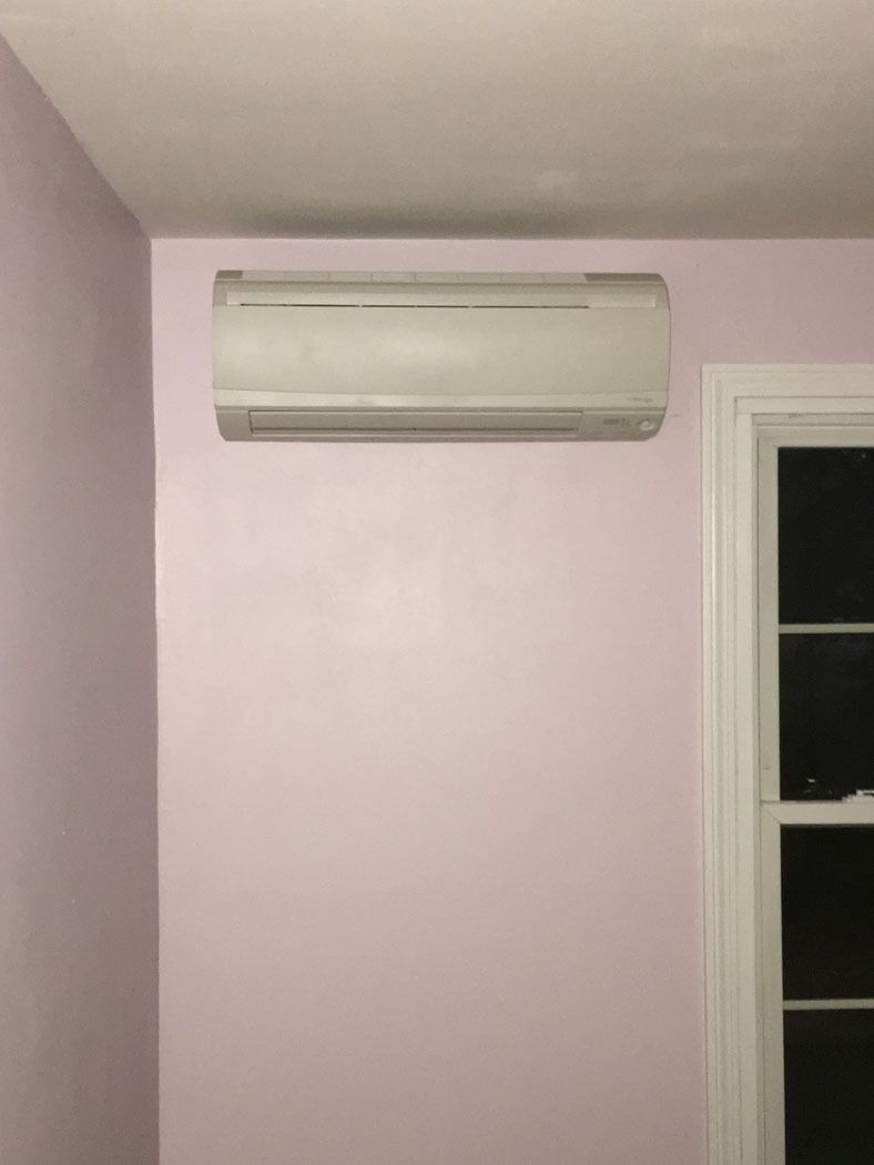 Wall-mounted white air conditioner above a lavender wall beside a window.