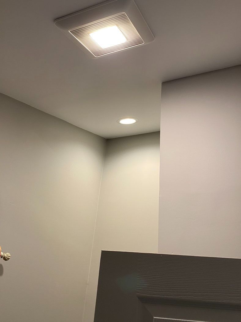 Ceiling corner with recessed lights and a wall-mounted panel in a plain gray room