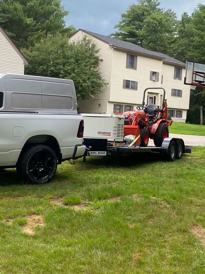 Pickup truck towing a flatbed trailer with a lawn tractor on grass in front of a house