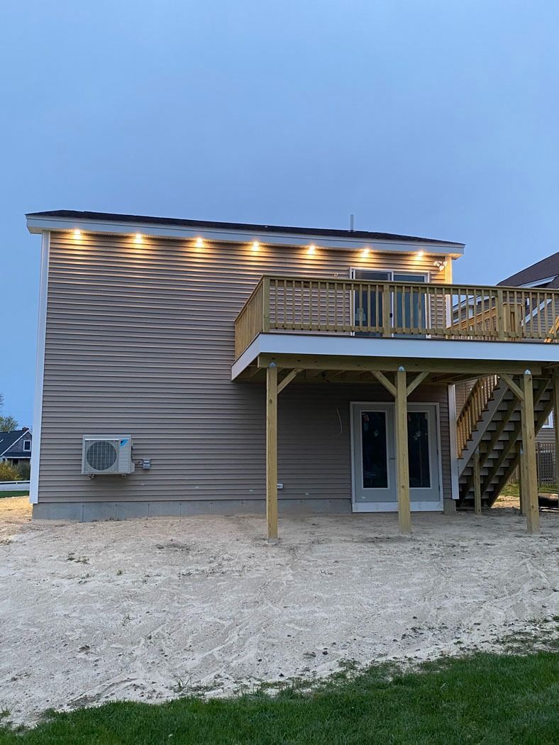 Two-story house exterior with gray siding, deck stairs, and wall lights at dusk