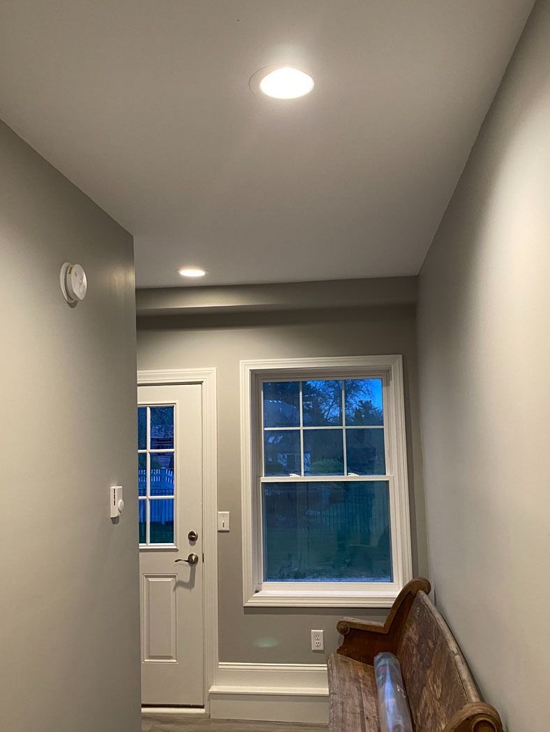 Narrow hallway with gray walls, white door and window, and a wicker bench by the window.