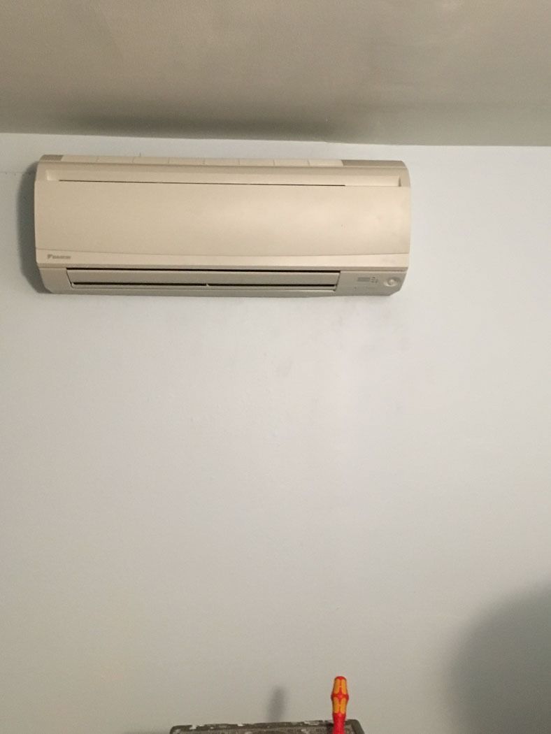 Wall-mounted beige air conditioner on a plain light gray wall, with a small orange object at the bottom.
