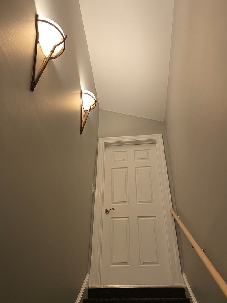 Stairwell with two wall lights, a wooden handrail, and a white door at the landing.