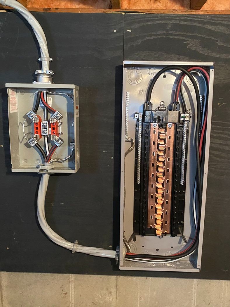 Open electrical breaker panel and small junction box with exposed wiring on a dark wall.