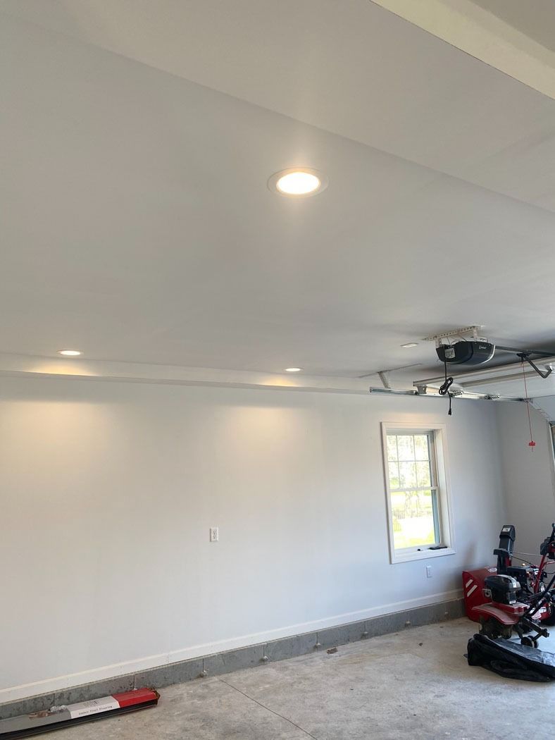 Empty white garage interior with recessed lights, a window, and tools near the right wall