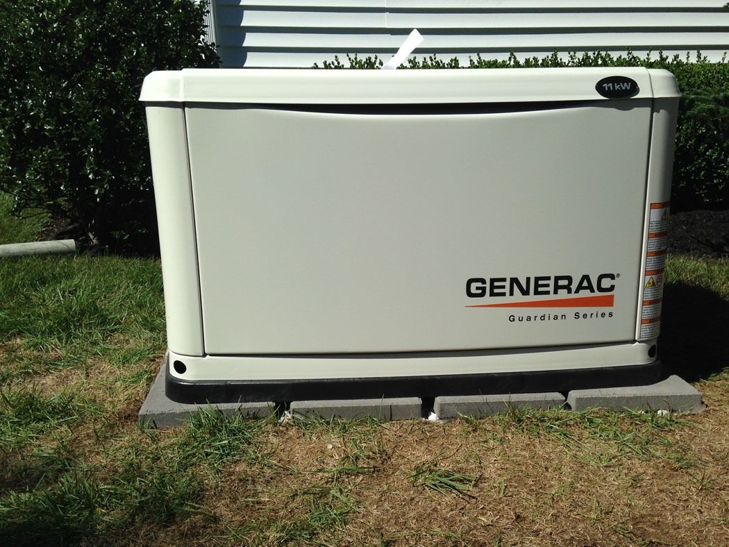 White Generac backup generator outdoors on a concrete pad beside grass and shrubs.
