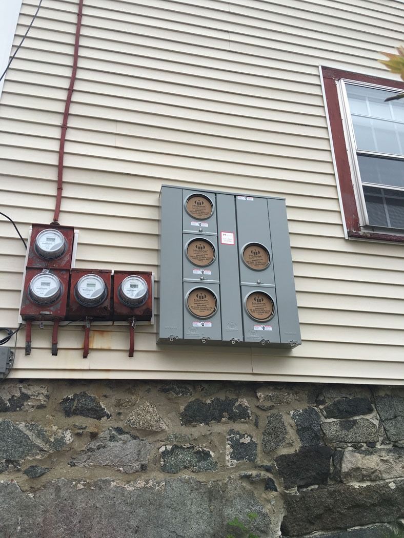 Electrical meters and utility boxes mounted on a house exterior wall beside a window.