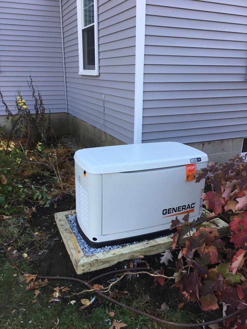 White home generator beside gray house siding on a concrete pad, partly covered by fallen leaves.