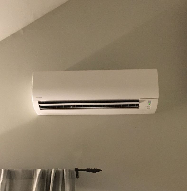 Wall-mounted white air conditioner on a beige wall above a curtain rod