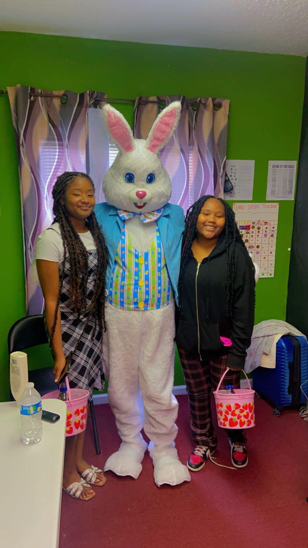 Two smiling individuals standing on either side of an Easter Bunny mascot inside a room with green walls.