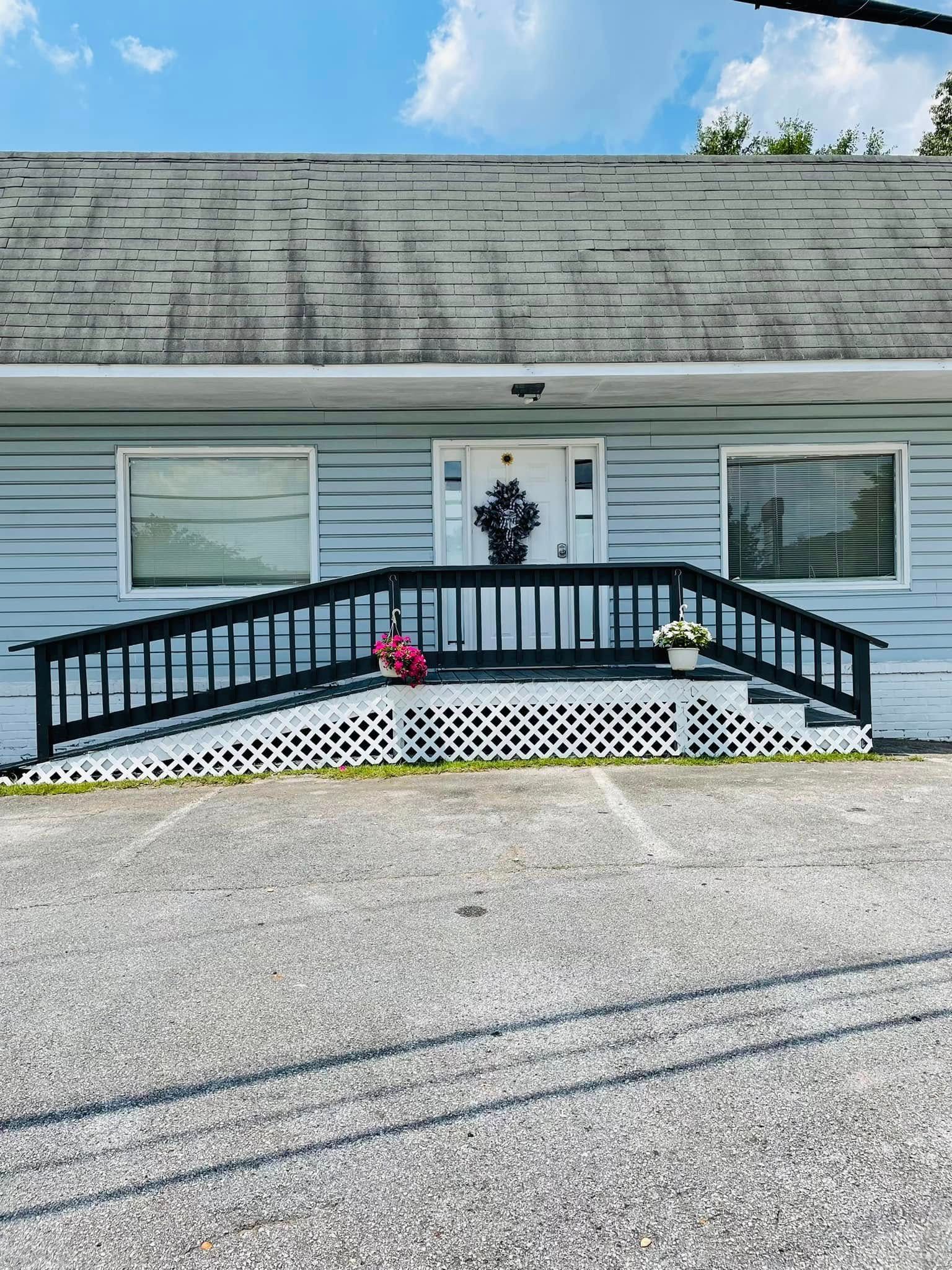 A building entrance with a black wooden wheelchair ramp and a white door with a decorative wreath in front of a gravel lot.