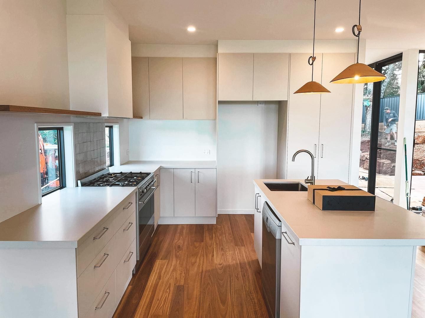 A kitchen with white cabinets , wooden floors , stainless steel appliances and a large island.