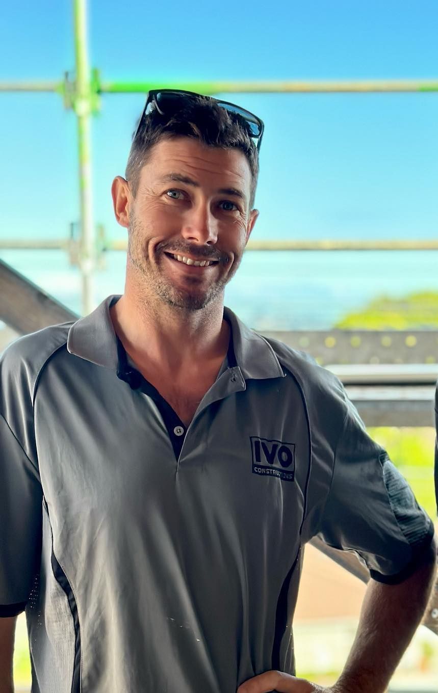 a man in a gray shirt is smiling and standing with his hands on his hips .