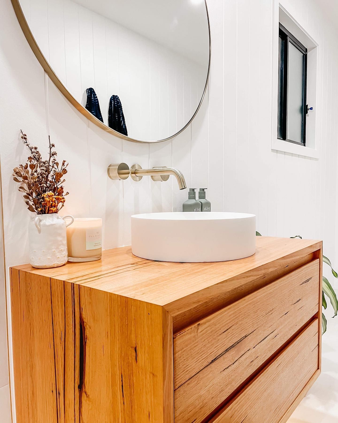 A bathroom with a wooden vanity , sink , mirror and window.