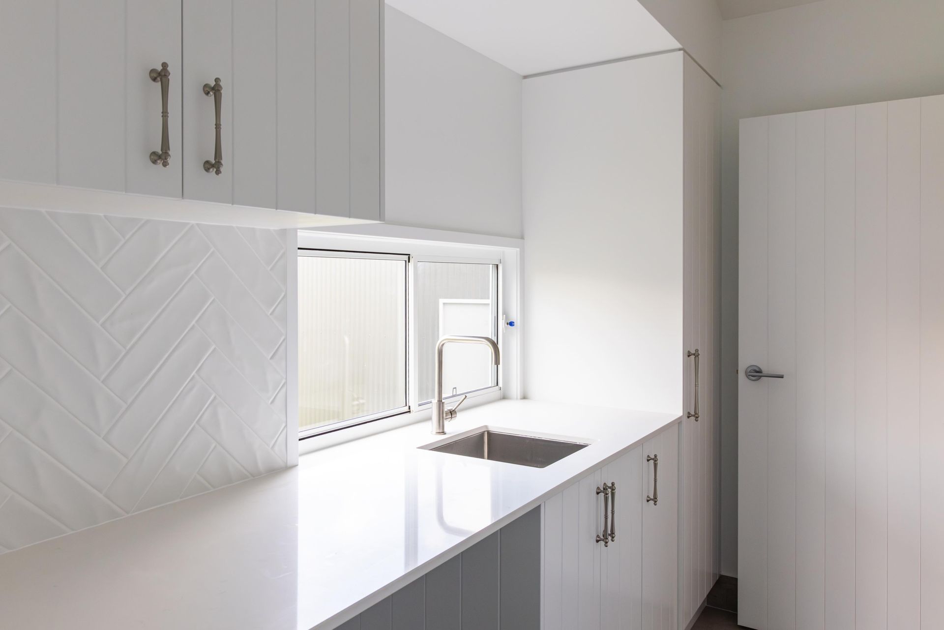 A kitchen with white cabinets , a sink , and a window.