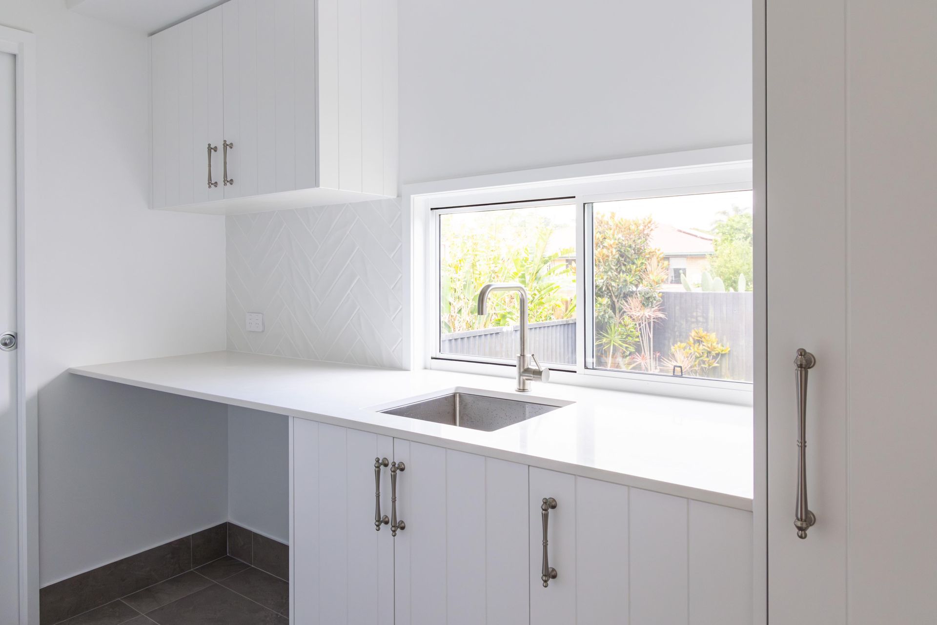 A kitchen with white cabinets , a sink , and a window.