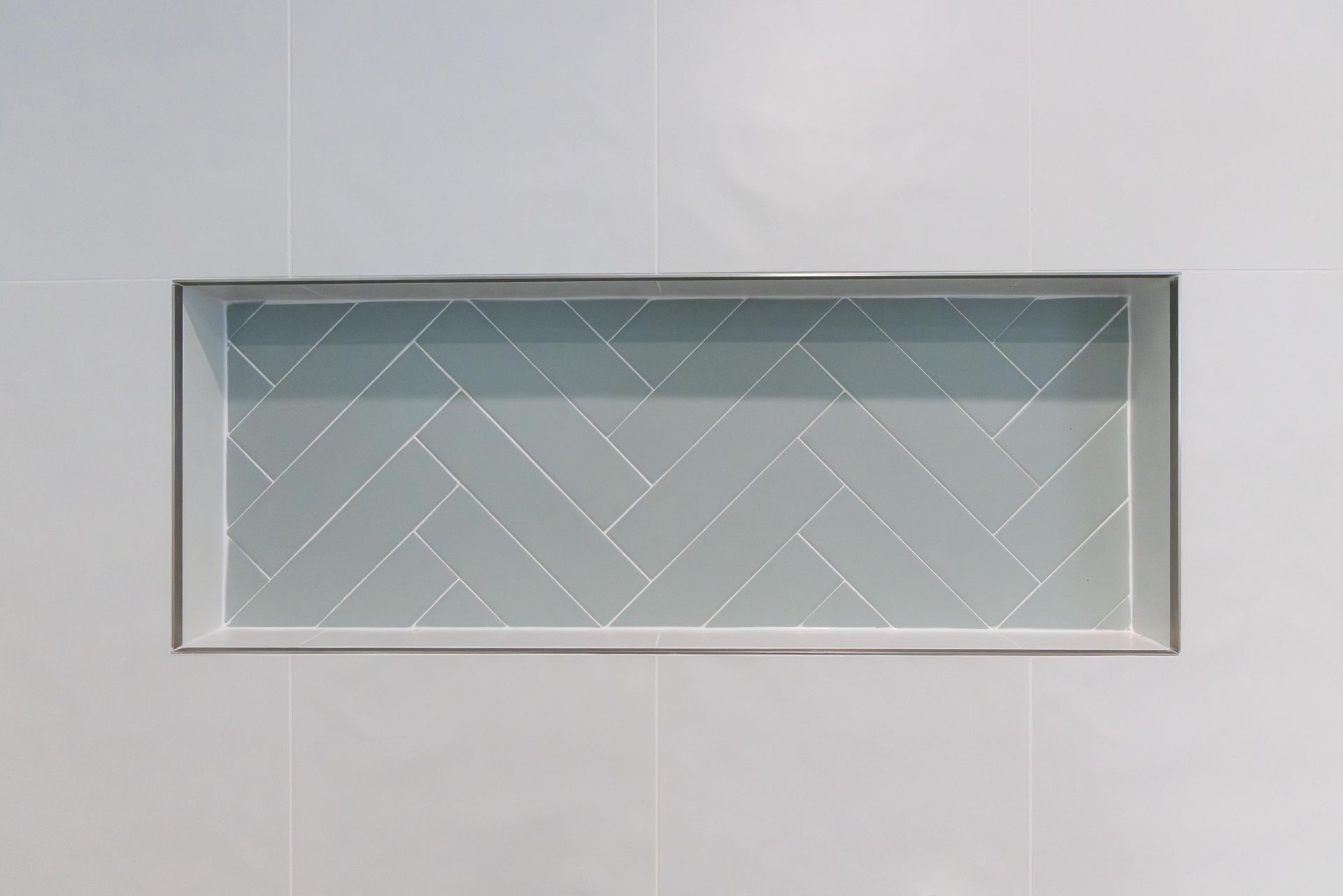 A shower niche with a herringbone pattern on a white wall.