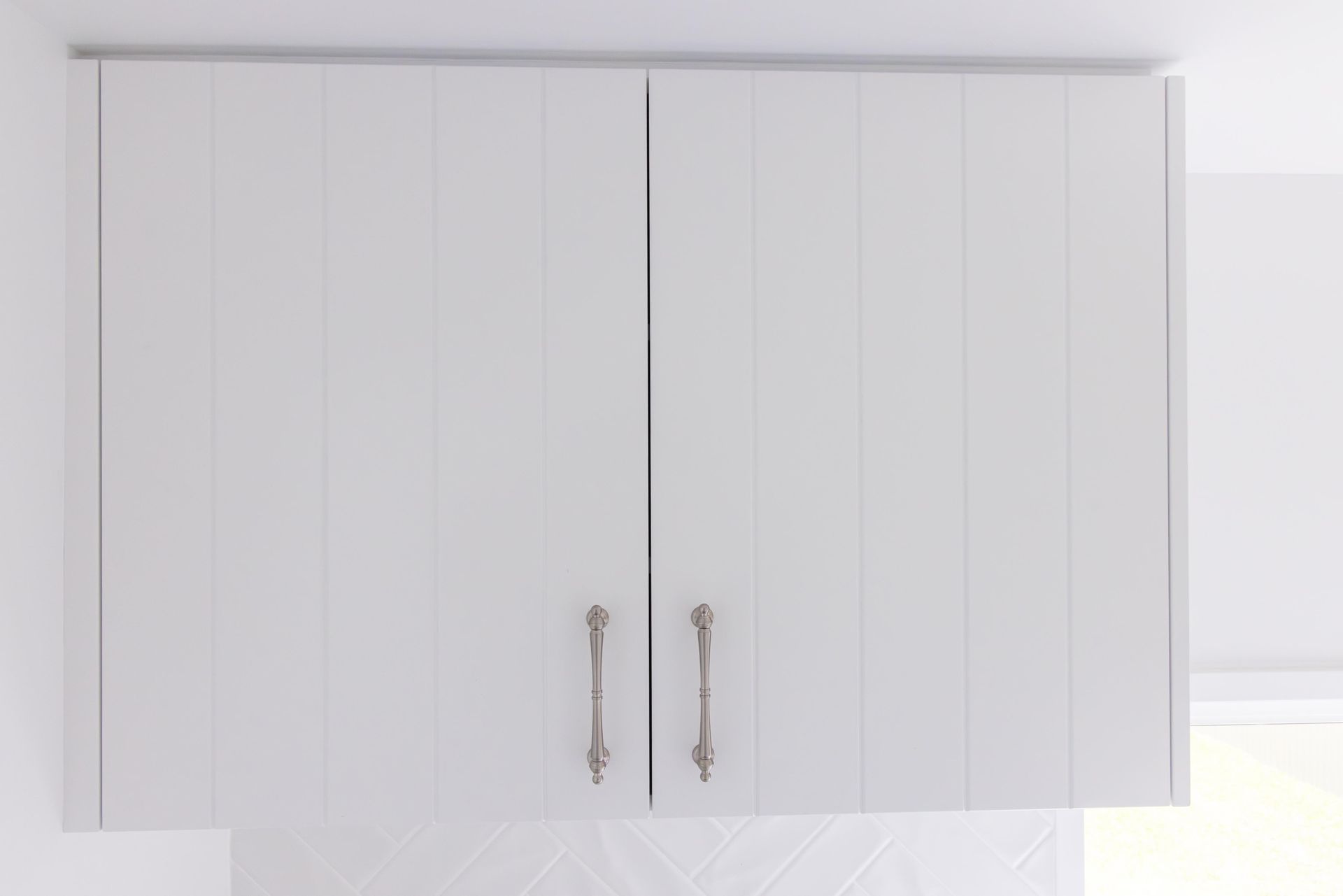 A white cabinet with two doors is hanging from the ceiling in a kitchen.