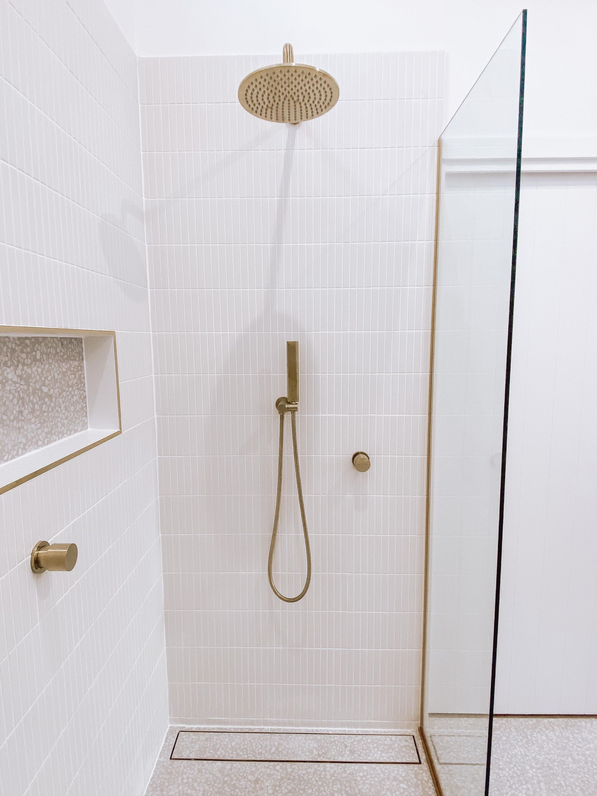A bathroom with a walk in shower and a brass shower head.