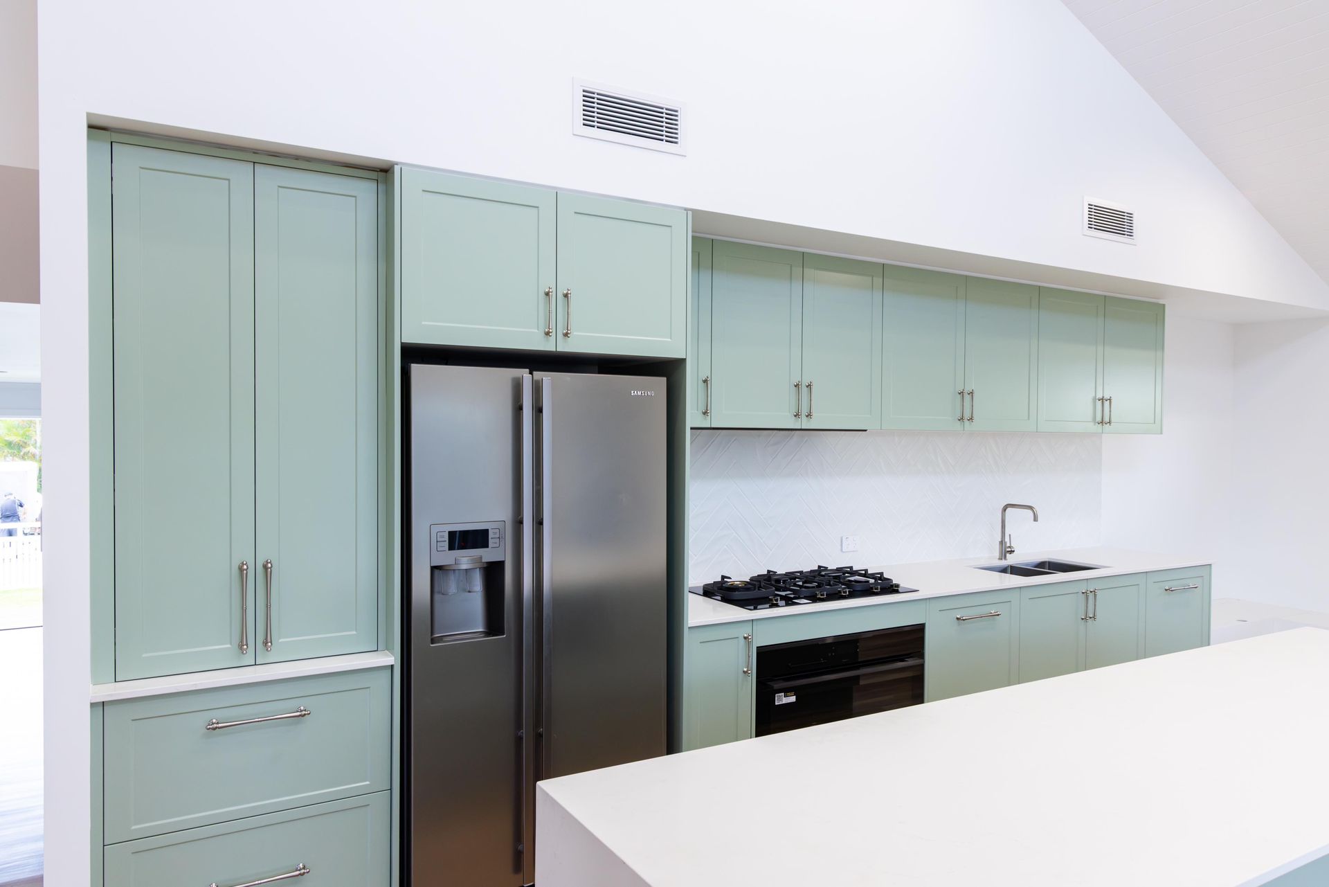 A kitchen with green cabinets and a stainless steel refrigerator