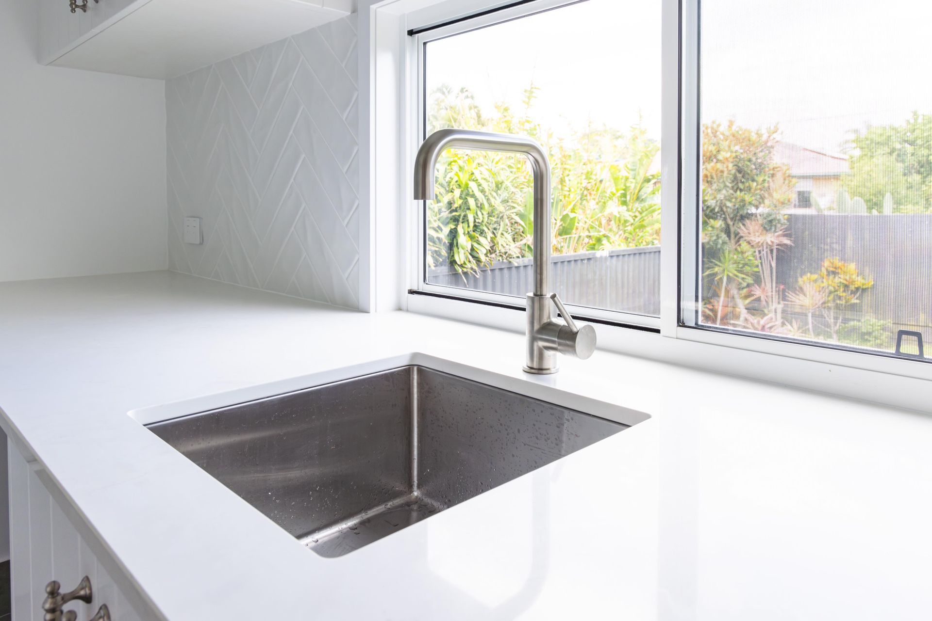 A kitchen sink with a faucet and a window in the background.