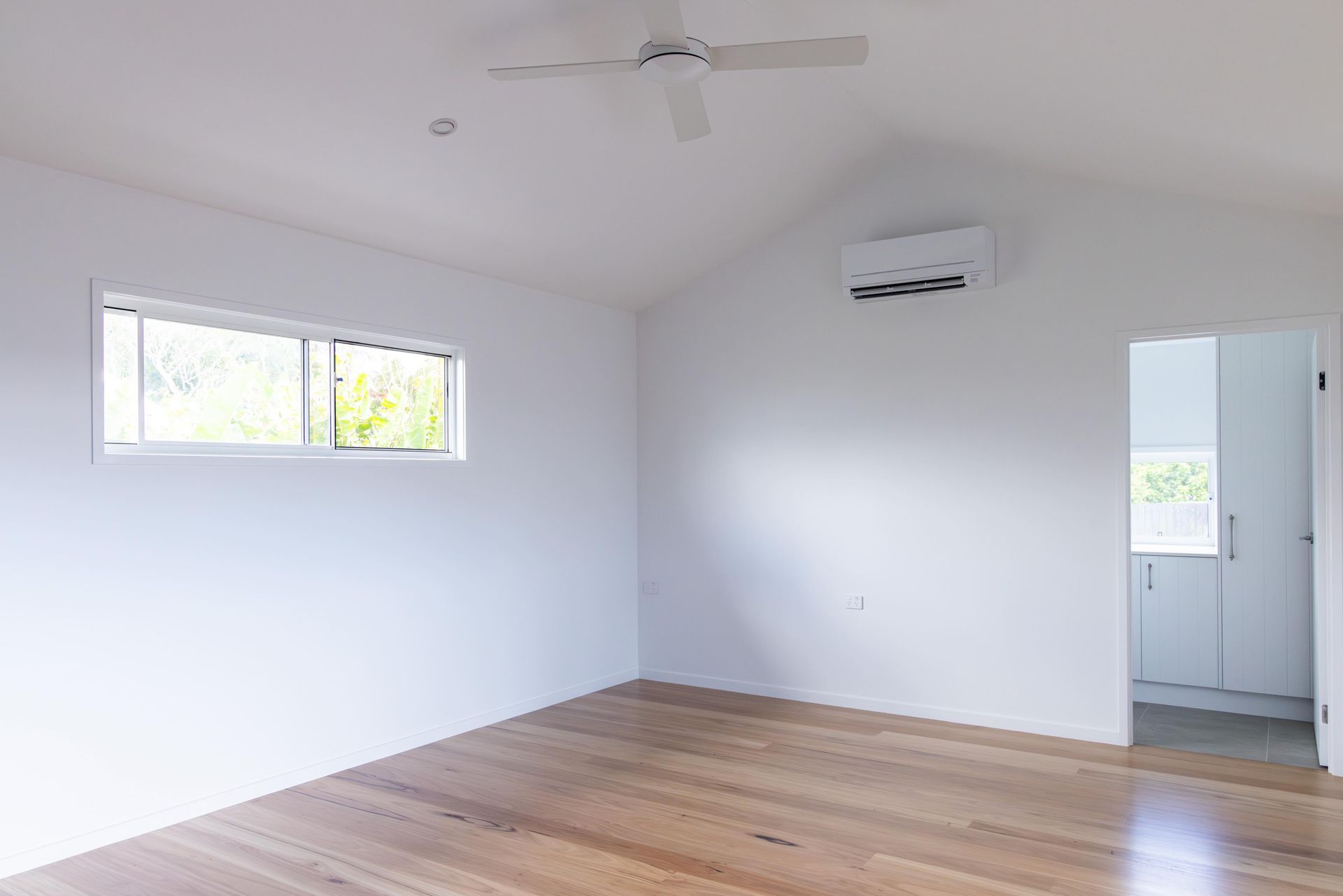 An empty room with hardwood floors , white walls and a ceiling fan.