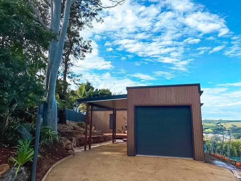 A garage with a black door is surrounded by trees on a hillside.