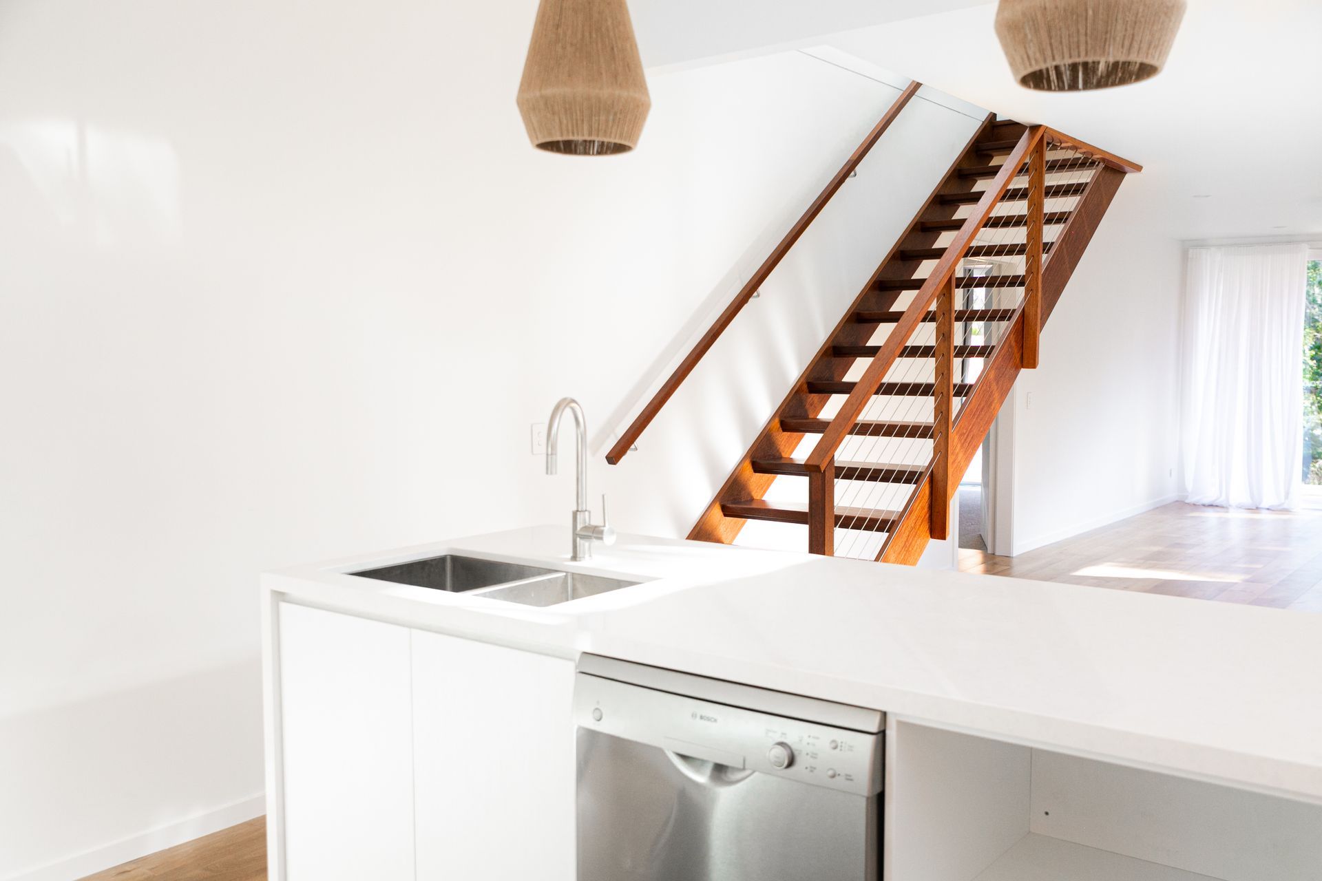 A kitchen with a sink , dishwasher , and stairs leading up to the second floor.