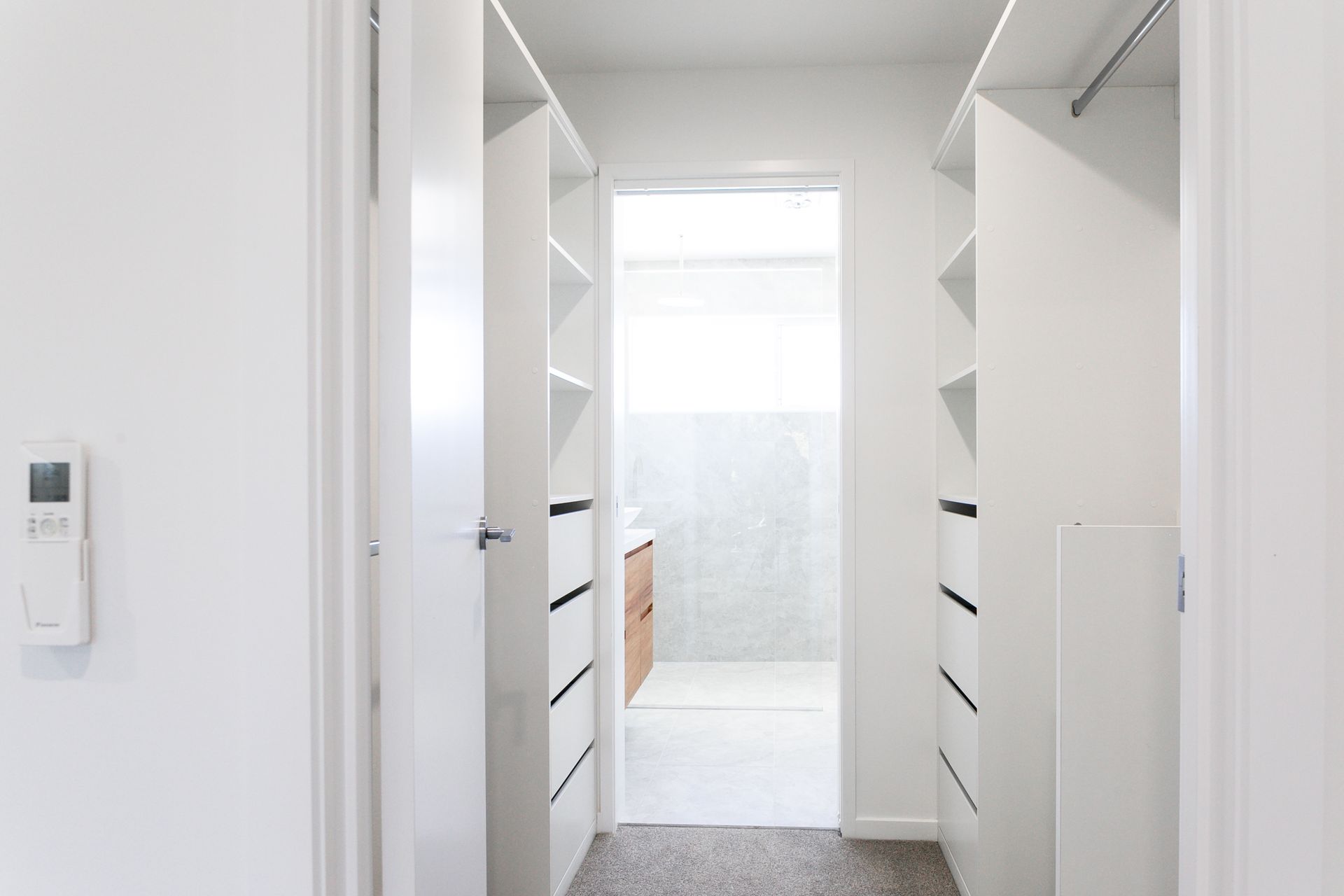 A walk in closet with lots of shelves and drawers leading to a bathroom.
