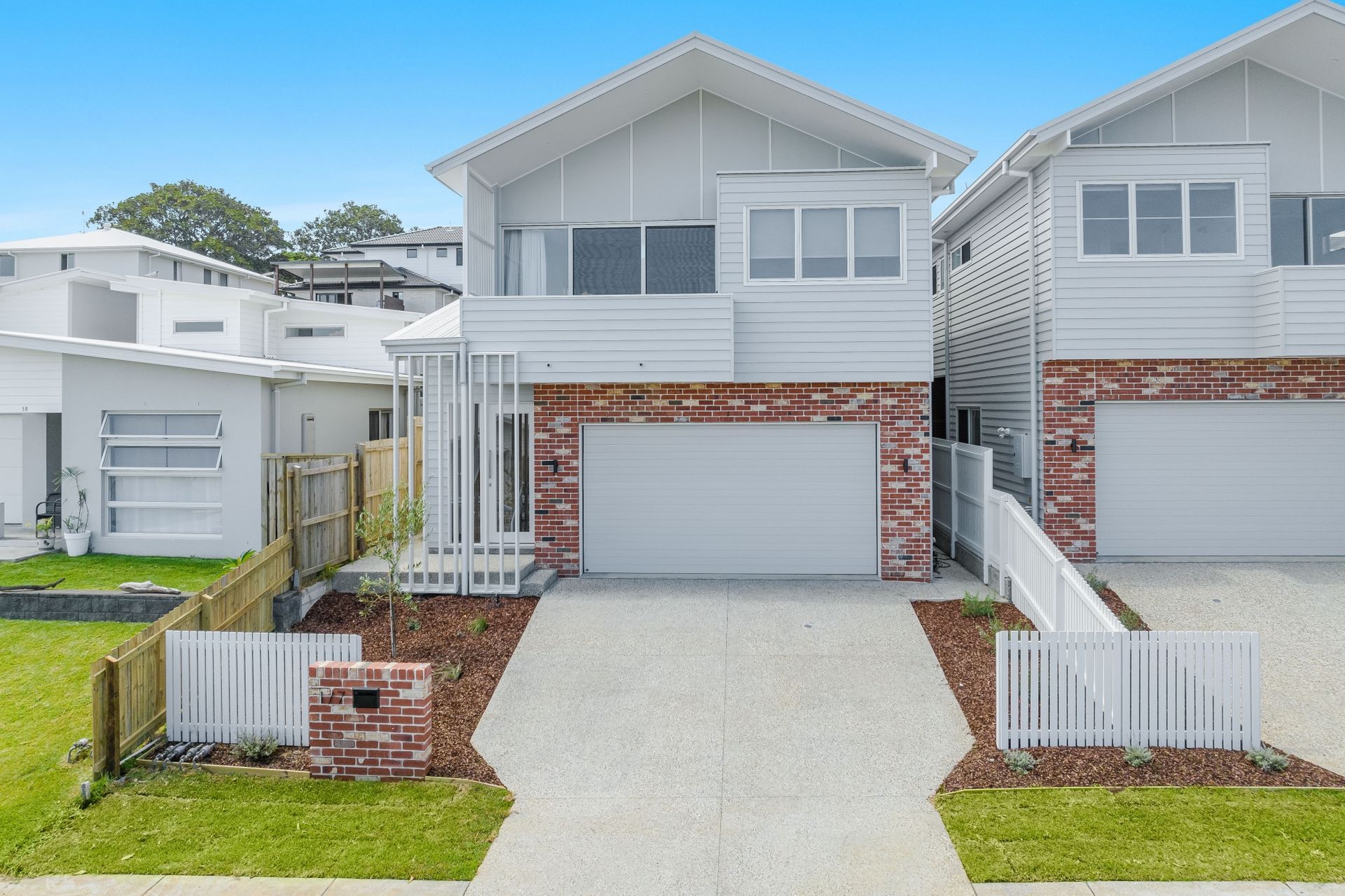 A white house with a red brick wall and a white garage door.