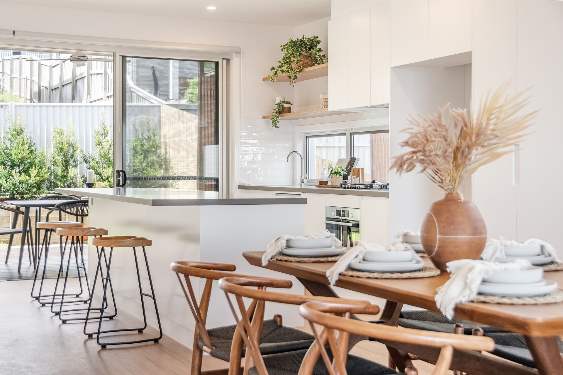 A dining room with a table and chairs and a kitchen in the background.