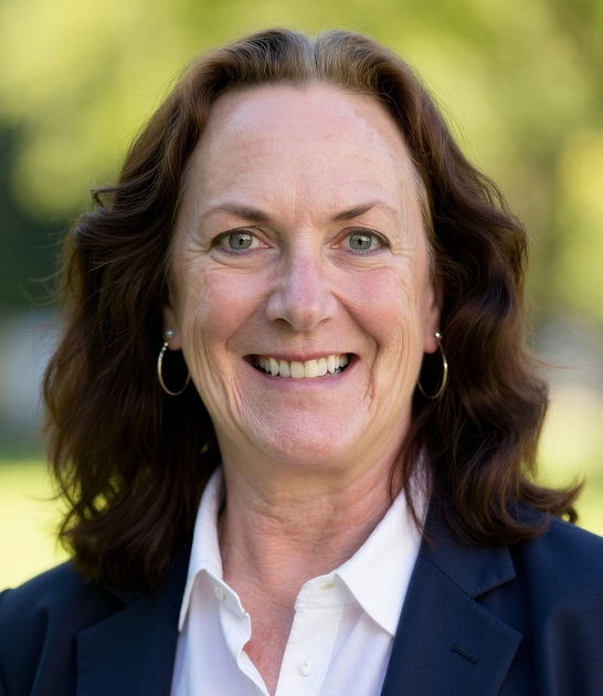 Smiling person in a navy blazer and white shirt against a blurred outdoor background