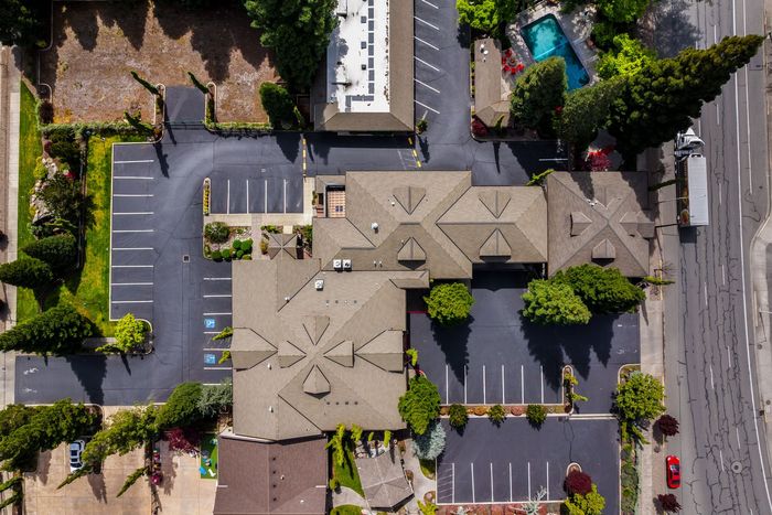 Aerial view of a tan-roofed apartment complex with parking lots, trees, and a road beside it